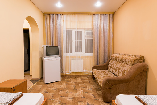 The interior of a small room with sofa bed and two single beds, window, TV and fridge