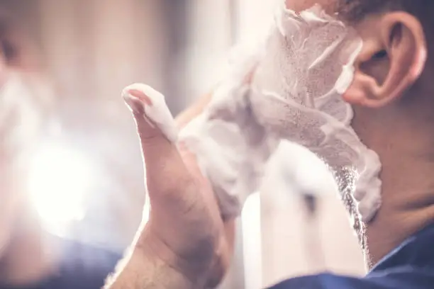 One man in the bathroom , Shaves his beard .