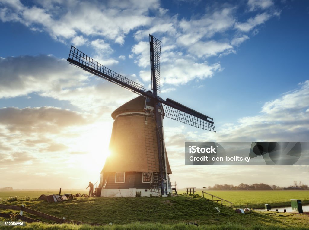 Windmill and silhouette of a man at sunrise in Netherlands Windmill and silhouette of a man at sunrise in Netherlands. Beautiful old dutch windmill against colorful sky with clouds. Spring landscape in the morning in Holland. Rural scene. Travel background Netherlands Stock Photo