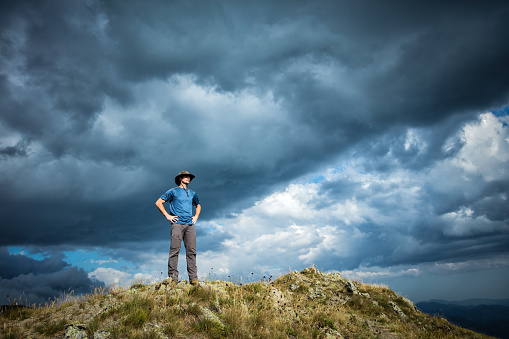 Man mountaineer standing on mountain and looking away under very dramatic cloudy sky