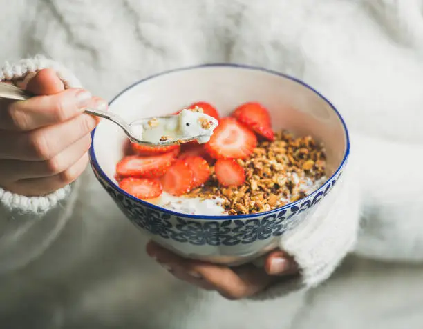 Photo of Healthy breakfast yogurt, granola, strawberry bowl in woman's hands