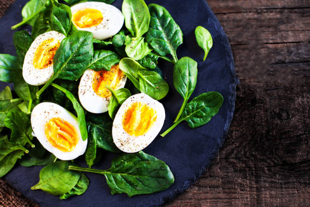 Fresh green spinach baby leaves and boiled eggs cut in a half on wooden background Fresh green spinach baby leaves and boiled eggs cut in a half on wooden background  with copyspace boiled egg photos stock pictures, royalty-free photos & images