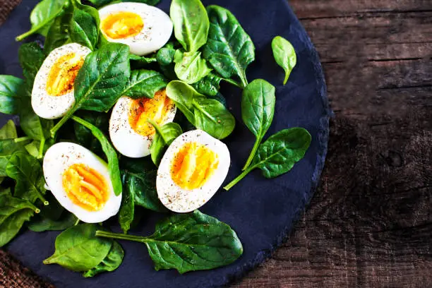 Fresh green spinach baby leaves and boiled eggs cut in a half on wooden background  with copyspace