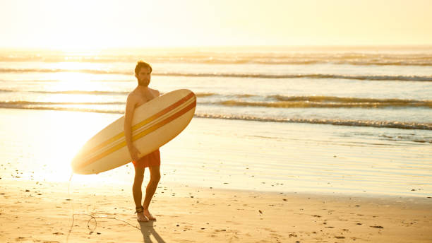 istock Male surfer walking on beach with surfboard at sunrise 642077158