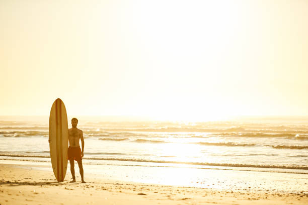 istock Surfer standing with his surfboard upright beside him on beach 642077180
