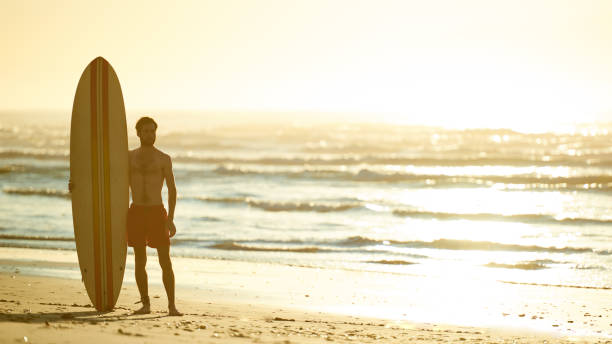 istock Surfer standing with his surfboard upright beside him on beach 642079236