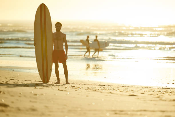 istock Surfer standing on beach with other surfers behind him 642079256