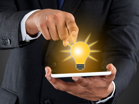 Businessman holding digital tablet and touching light bulb icon on touch screen