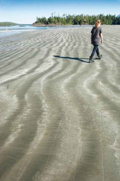 tofino, colúmbia britânica, canadá - 16 de julho de 2015: adolescente passeios através de uma ampla praia com areia ondulada do recuo água na maré baixa na praia mackenzie na ilha de vancouver - receeding - fotografias e filmes do acervo