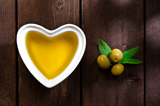 Healthy eating concept: Top view of a heart shaped bowl filled with olive oil shot on rustic wood table. Some olives are out of the bowl directly on the table. DSRL studio photo taken with Canon EOS 5D Mk II and Canon EF 100mm f/2.8L Macro IS USM