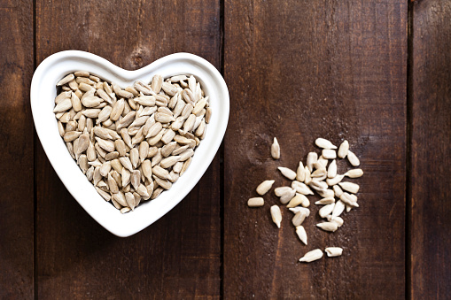 Healthy eating concept: Top view of a heart shaped bowl filled with peeled sunflower seeds shot on rustic wood table. Some seeds are out of the bowl directly on the table. DSRL studio photo taken with Canon EOS 5D Mk II and Canon EF 100mm f/2.8L Macro IS USM