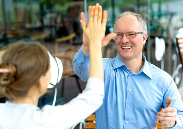 Closeup of smiling middle-aged man and woman giving high five with cafe interior in background
