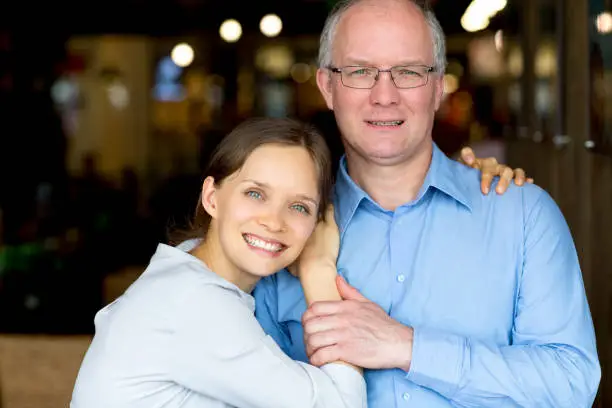 Closeup of smiling young woman embracing middle-aged man. They are looking at camera.