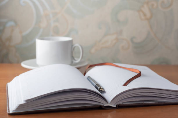istock Open diary and pen businessman lying on a wooden table next to a white cup. Desktop. 642195930