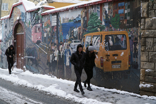 A famous street from Istanbul Kadikoy in a snowy day with a cute smiling young couple and a beautiful wall art.