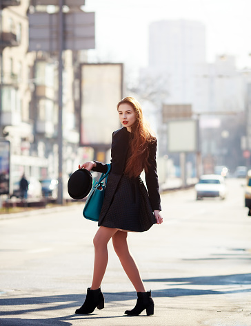 Beautiful fashionable woman in a hat and coat posing outside in a city street