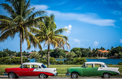 HDR - Two american red green white vintage cars parked under palms near the water in Varadero Cuba - Serie Cuba Reportage