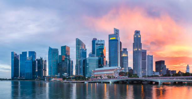 skyline von singapur an der marina bay in der dämmerung mit glühenden sonnenuntergang beleuchtet die wolken - singapore stock-fotos und bilder