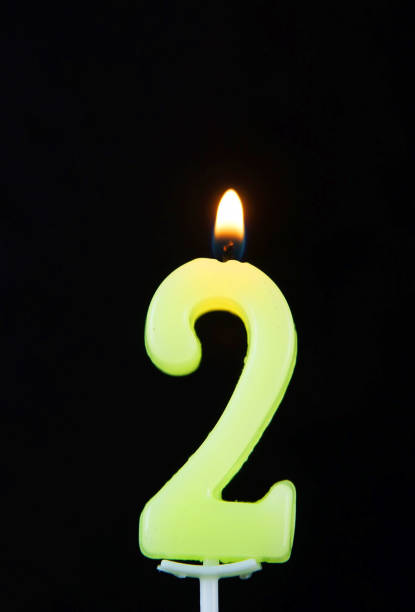 istock Burning wax candle as number two on black background 642262202