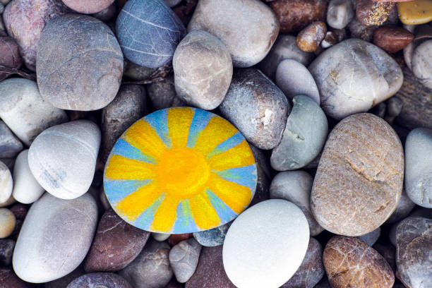 Bright sun painted on pebble with stones background stock photo