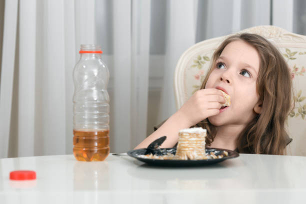 Small blonde girl sits at table eating a cake with her hands