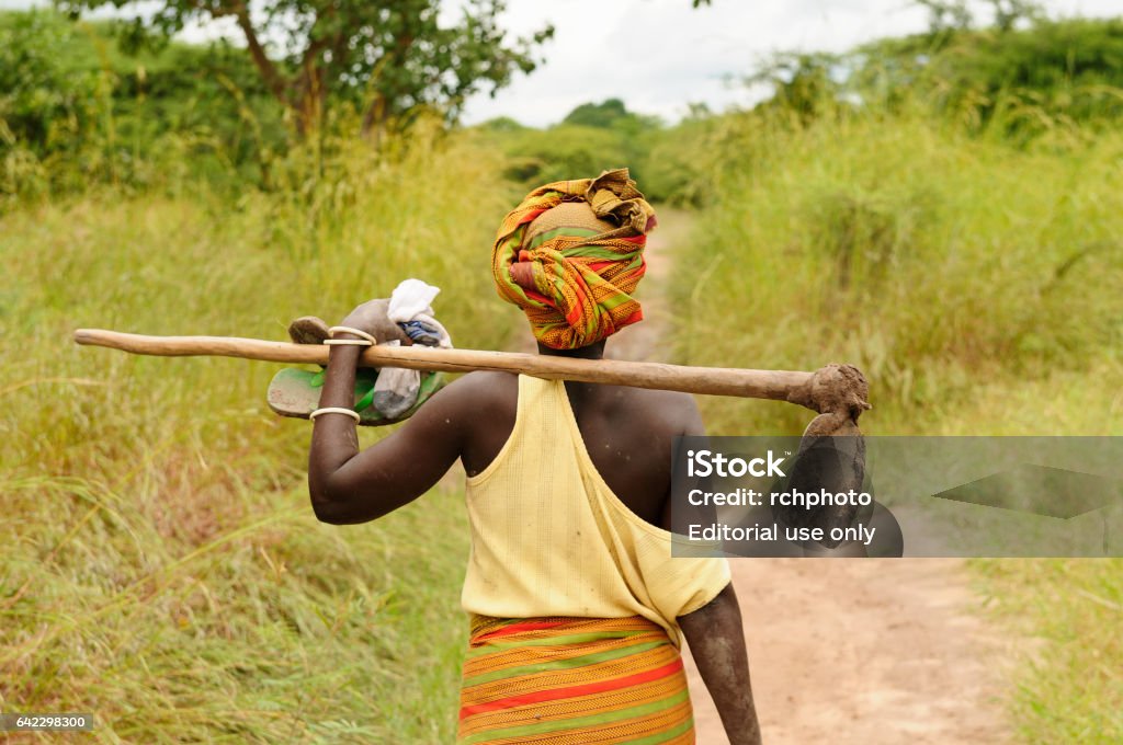 African woman African woman with the turban on the head going dirt road to work with the hoe in field in Tanzania Africa Stock Photo