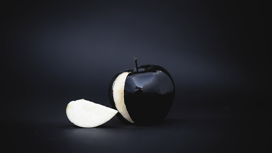 sliced black apple on a black background with a slice