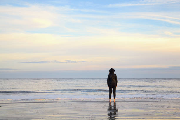 istock Young woman in hat standing on ocean beach on sunset 642355976