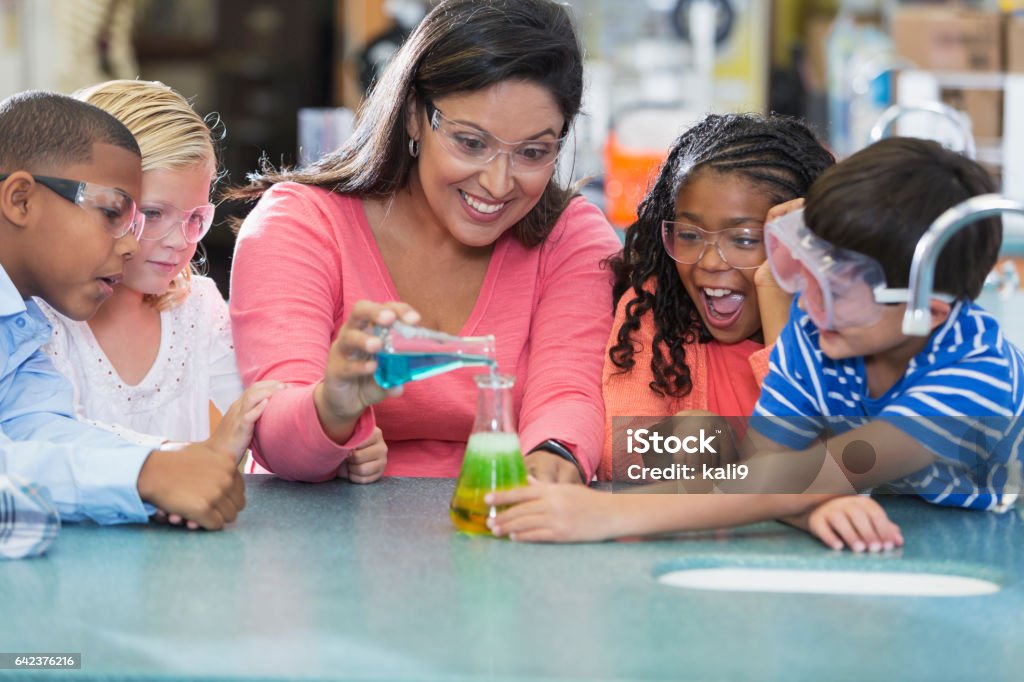 Multi-ethnic teacher and children in science lab An Hispanic woman in her 40s teaching a multi-ethnic group of elementary school students in science lab. They are doing an chemistry experiment with colorful liquids in beakers. Science Stock Photo