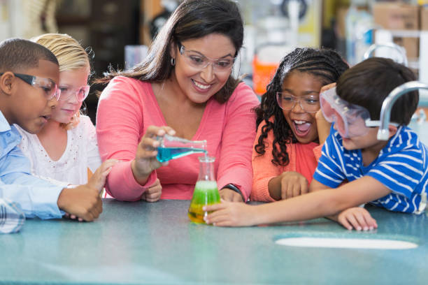 Multi-ethnic teacher and children in science lab An Hispanic woman in her 40s teaching a multi-ethnic group of elementary school students in science lab. They are doing an chemistry experiment with colorful liquids in beakers. science class stock pictures, royalty-free photos & images