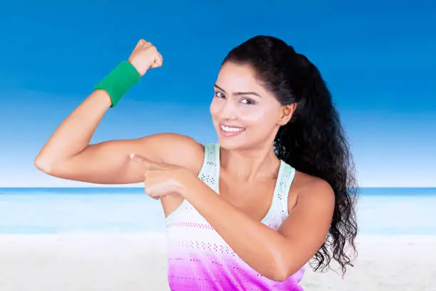 Portrait of beautiful woman pointing her muscle while standing at the beach