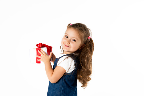 Cute little girl is holding a red gift box in her hands an is looking at camera with a nice smile.