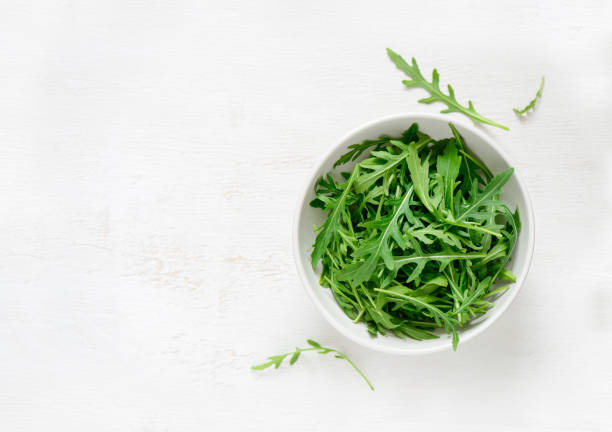 Arugula in a white bowl Fresh arugula leaves in a white bowl, view from above, space for a text arugula stock pictures, royalty-free photos & images