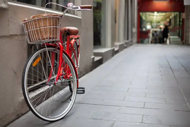 A shoppers red commuting bicycle with basket is parked in a laneway in Melbourne, Australia, with shops in the background.