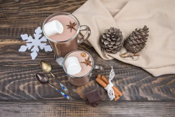 Two glass cup of hot chocolate or cocoa with marshmallows, cinnamon and anise on dark wooden background. Christmas drink