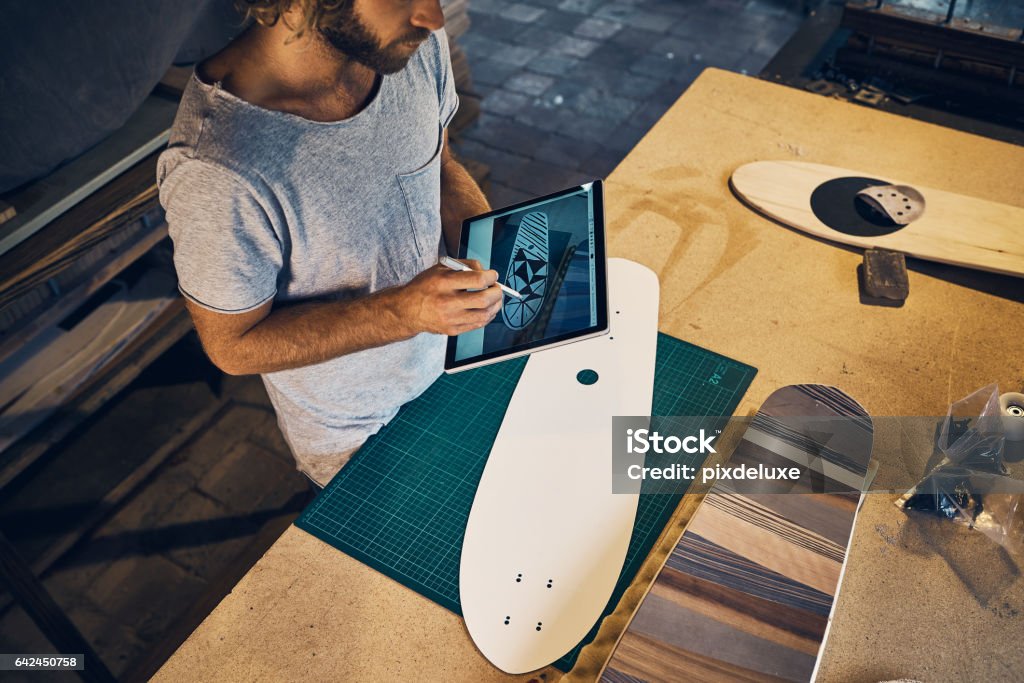 Designing a deck that will inspire envy Shot of a young man designing a skateboard on his tablet in the workshop Customized Stock Photo