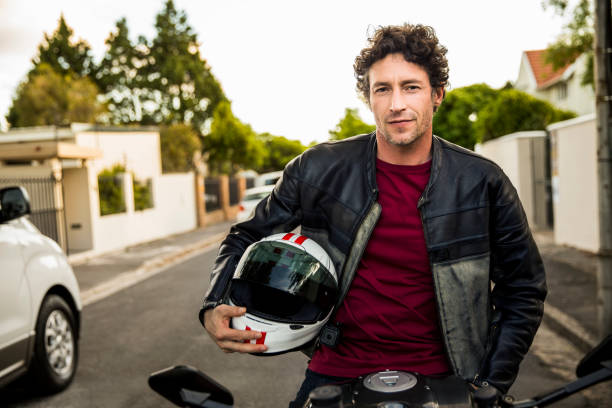 Confident man sitting on motorcycle Portrait of confident man sitting on motorcycle. Mature male is holding crash helmet. He is wearing leather jacket on street. crash helmet photos stock pictures, royalty-free photos & images