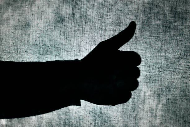 the shadow of a man giving a thumbs-up sign behind a gray fabric