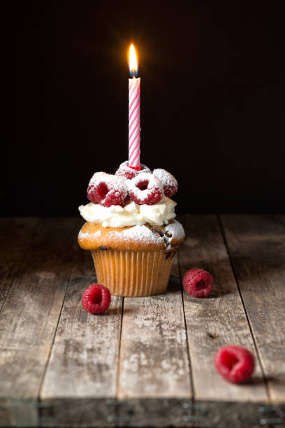 Birthday cupcake with a candle in the form of a heart on a wooden board with raspberries on a gray background close -up