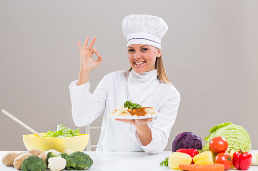Cheerful female chef is showing ok sign while holding prepared meal.