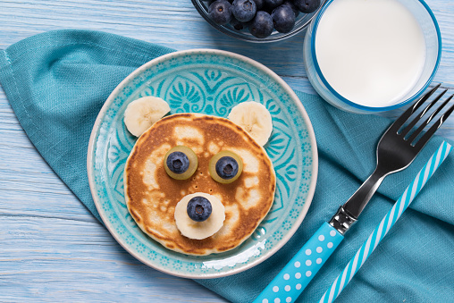 Funny pancake in a shape of teddy bear, food for kids idea, blue wooden background, top view