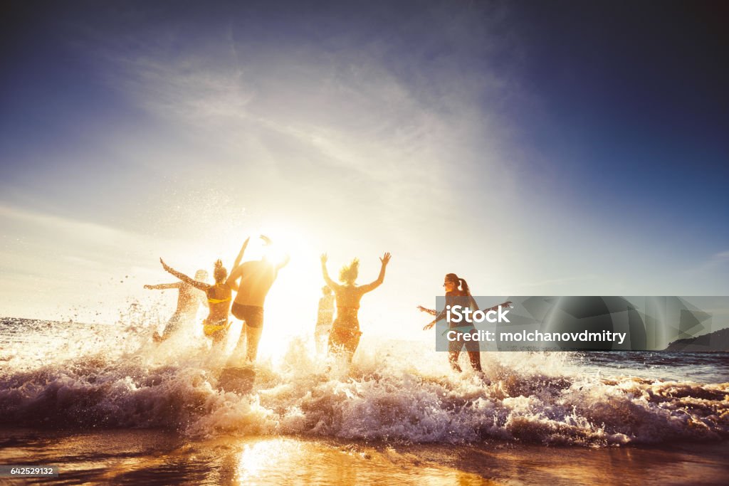 Big group friends sun beach travel Big group of friends runs in sun light at the beach into the sea. Travel concept. Space for text Beach Stock Photo