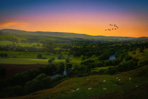 Photo of Sunset over mountains and meandering River making its way through lush green rural farmland in England.