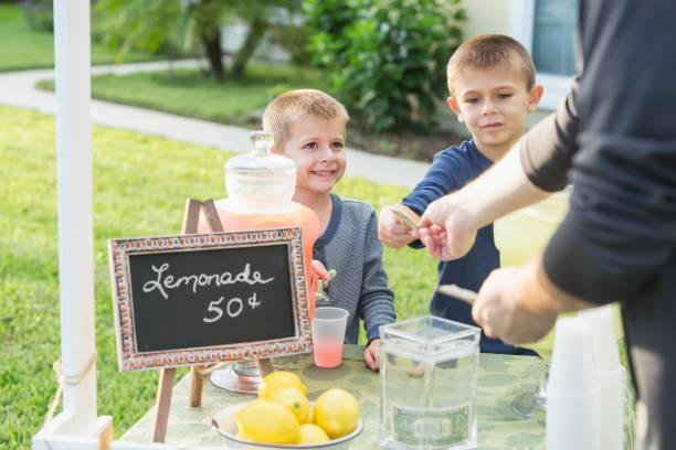 Boys with lemonade stand, taking payment from man Two boys selling lemonade in their front yard. They are serving pink lemonade to a customer, cropped so only his arms are visible, he is handing cash to the older brother. images of lemonade stands stock pictures, royalty-free photos & images