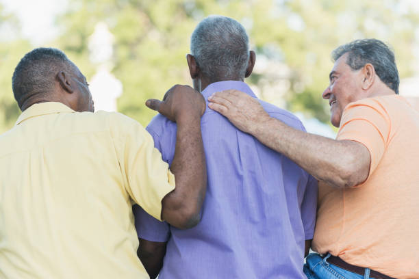 Three multi-ethnic senior men sitting on bench Rear view of three multi-ethnic senior men sitting together on a park bench. The two men on the ends seem to be comforting their African American friend sitting between them. hand on shoulder stock pictures, royalty-free photos & images