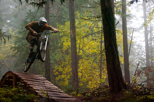 A man jumps off a wooden bridge on his downhill mountain bike on a foggy day in British Columbia, Canada.