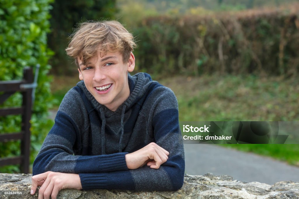 Young happy laughing smiling teenager male boy blond child outside leaning on a wall in autumn fall sunshine Teenage Boys Stock Photo