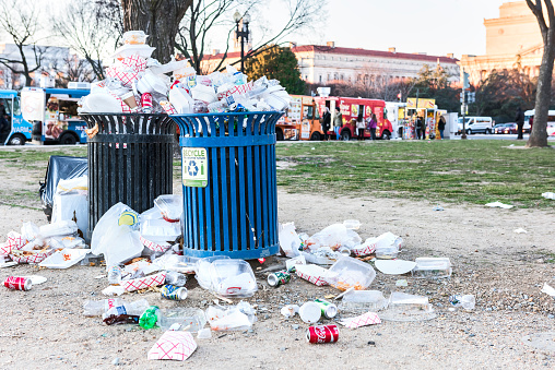 Overflowing trash bins in National Mall with people eating by food trucks