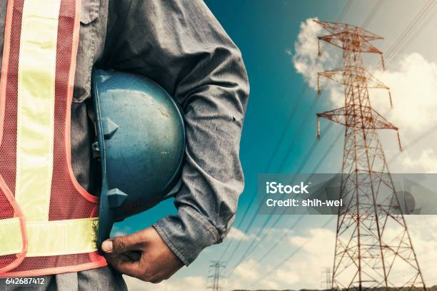 Engineer Holding Blue Helmet Standing On Highvoltage Tower Stock Photo - Download Image Now