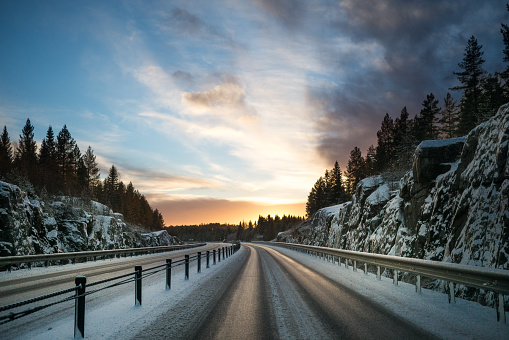 Vinterväg i Sverige med solen som går upp i horizonten med berg och snö vid sidan av vägen. Vackra färger i soluppgången.